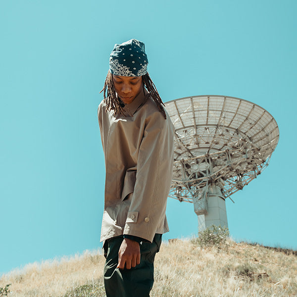 Model wearing a black Bardo jacket and trousers with a white shirt beneath a large satellite dish.
