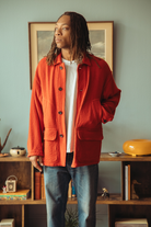 Man wearing a red coat standing in front of a blue wall.